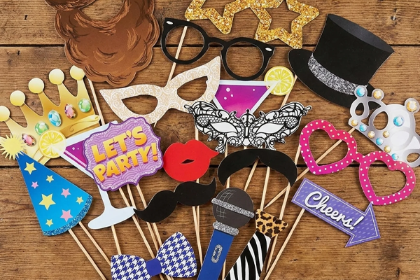 Samling af farverige photo booth rekvisitter på pinde — krone, hat, maske, briller, overskæg, læber, butterfly, mikrofon og skilte med "Let's Party!" og "Cheers!". Perfekte rekvisitter til selfie circle og photo booth.