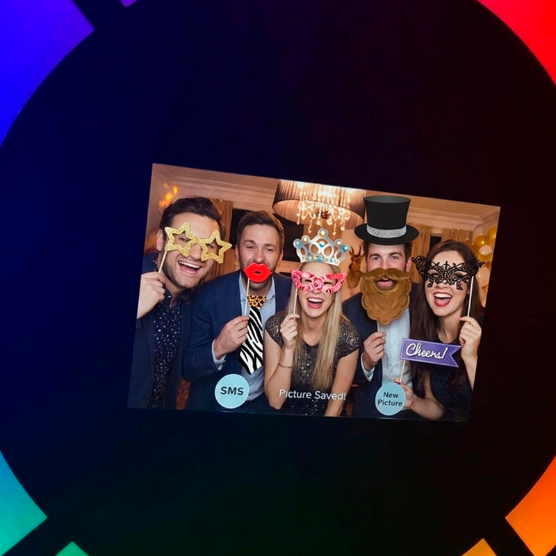 Claude responded: Fem gæster griner og poserer med rekvisitter ved en selfie circle photo booth — stjerne-briller, krone, hat, bart og maske.Fem gæster griner og poserer med rekvisitter ved en selfie circle photo booth — stjerne-briller, krone, hat, bart og maske. Skærmen viser "Picture Saved!" med mulighed for at dele via SMS. Selfie circle med ringlys i baggrunden.